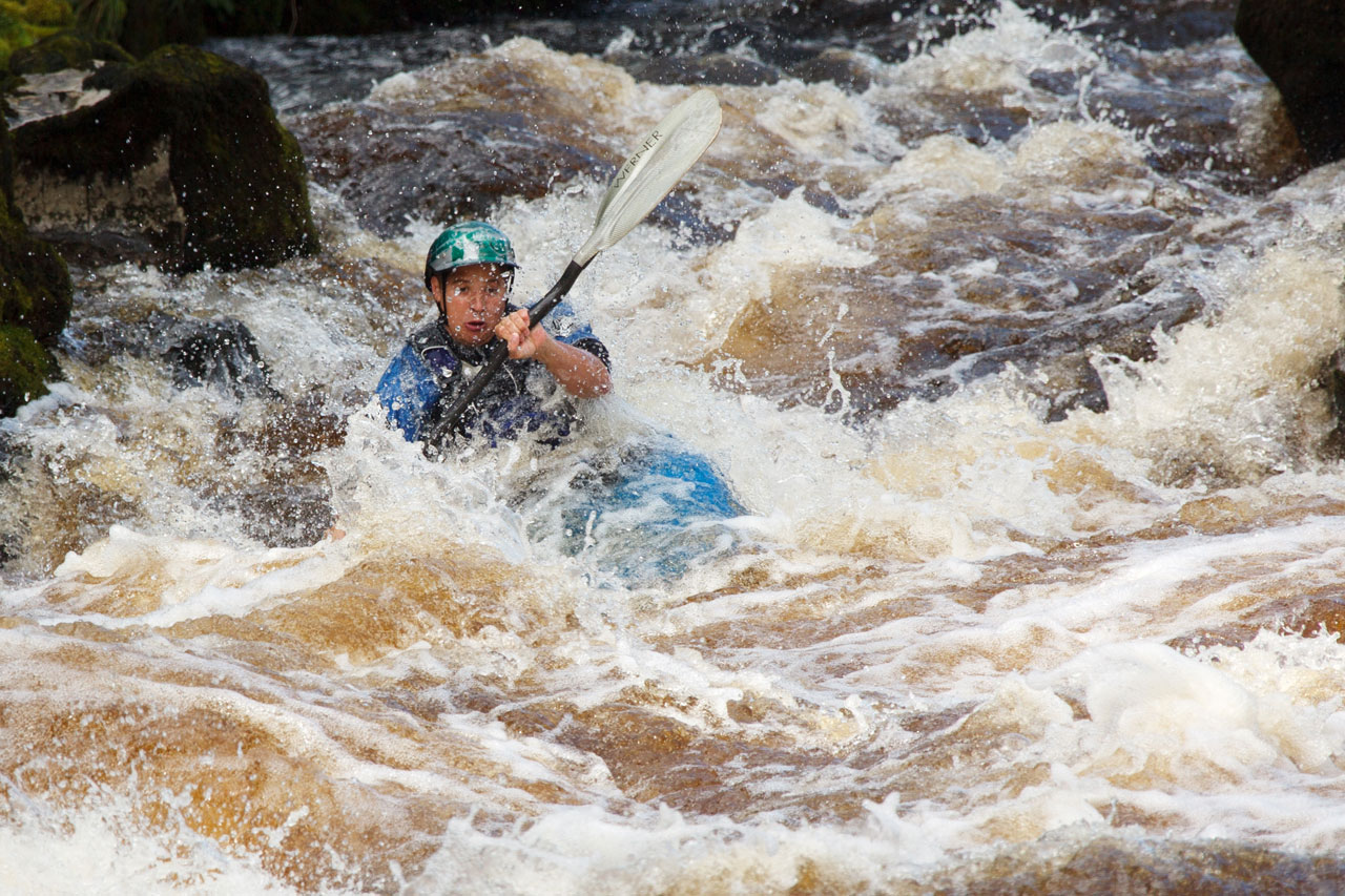Man kayaking in whitewater engaging core