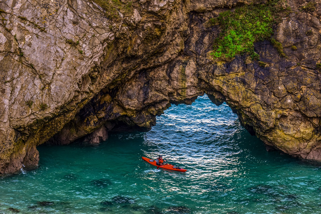 Person kayaking under a natural rock formation, water reflecting the rocks