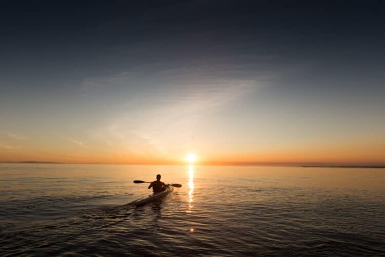 kayaker paddling against a vibrant sunset over the ocean