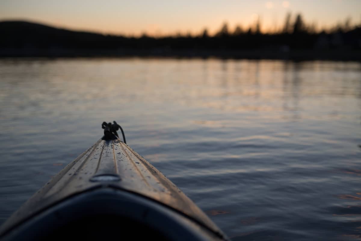 Close-up of a kayak's bow against the serene backdrop of a calm lake during sunset