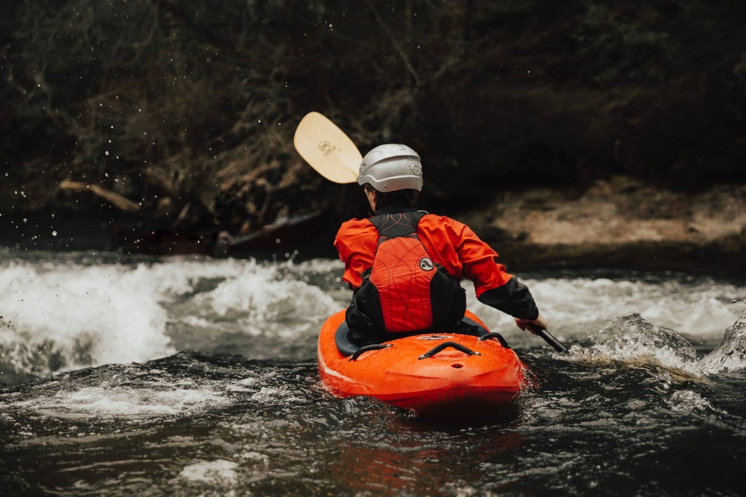 Kayaker in red gear navigating whitewater rapids